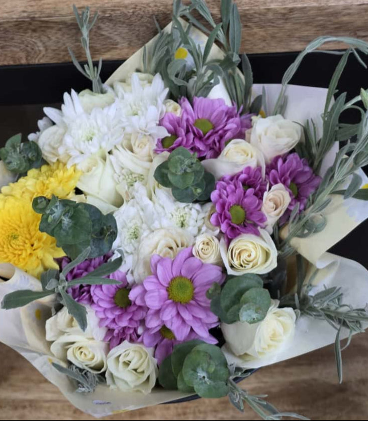 Bouquet of flowers with white, purple, and yellow flowers on a wooden surface