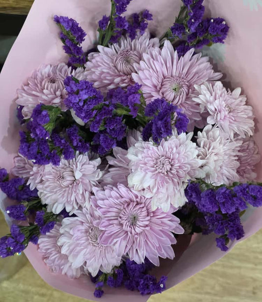 VeryKenyan Bouquet of pink and purple flowers in a pink paper wrap on a wooden surface.